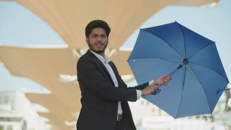 Young-dark-haired-muslim-man-testing-blue-umbrella-outside.