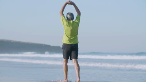 Mature-man-walking-along-ocean-coast-and-raising-arms-up