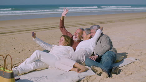 Cute-senior-friends-lying-on-shore-ant-taking-selfie-on-phone