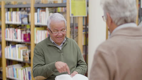 Fröhlicher-älterer-Mann,-Der-Mit-Einem-Freund-In-Der-Bibliothek-über-Ein-Buch-Spricht