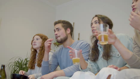 Amigos-Viendo-Televisión,-Bebiendo-Cerveza-Y-Apoyando-Al-Equipo-En-Casa