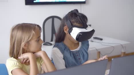 Schoolgirl-in-VR-headset-sitting-at-desk-near-classmate