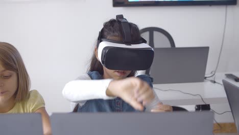Girl-in-VR-headset-sitting-at-desk-near-classmate