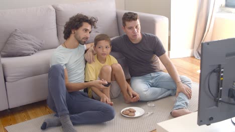 Glückliche-Schwule-Eltern-Und-Sohn,-Die-Kekse-Essen-Und-Filme-Schauen