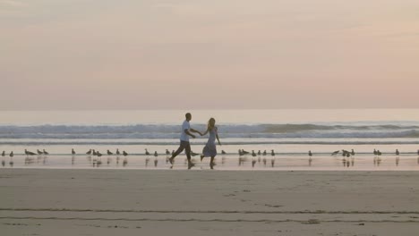 Romantic-Caucasian-couple-running-along-beach,-holding-hands.