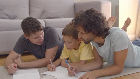 Focused-relaxed-fathers-and-son-lying-on-floor-and-drawing
