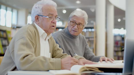 Focused-senior-men-writing-abstract-in-notebook-in-library