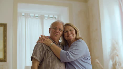 Front-view-of-happy-senior-couple-hugging-and-looking-at-camera