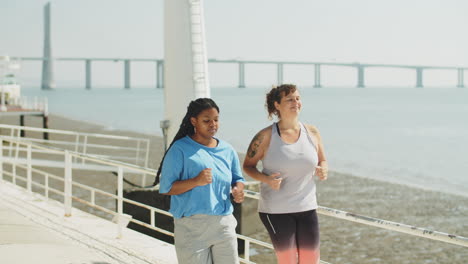 Long-shot-of-happy-women-jogging-along-embankment