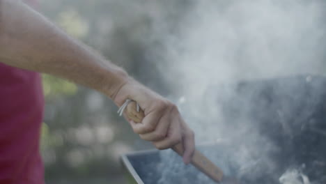 Close-up-of-male-hand-holding-spatula-over-barbeque-grill