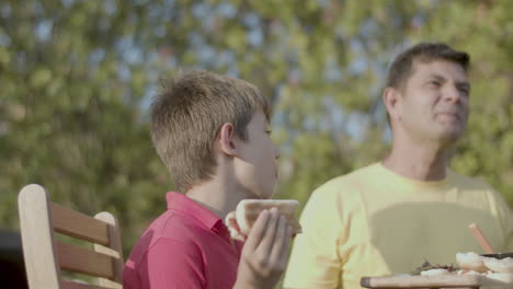 Preteen-boy-eating-hotdog-with-family-outdoors