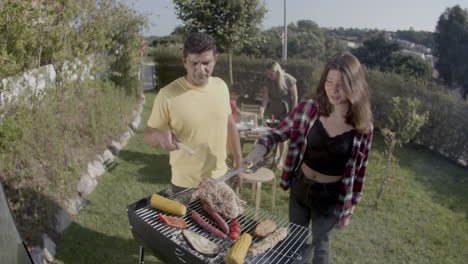 Smiling-teenage-daughter-cooking-meat-with-father-on-grill