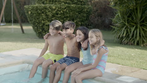 Children-sitting-on-pool-edge-dangling-their-feet-in-water.
