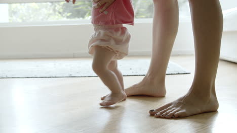 Cute-barefoot-baby-learning-walking-with-help-of-mother-on-floor