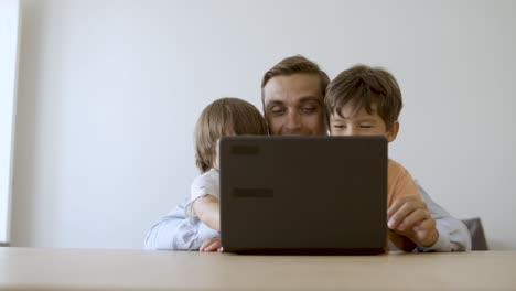 Middle-aged-dad-hugging-sons-and-playing-online-game-on-laptop