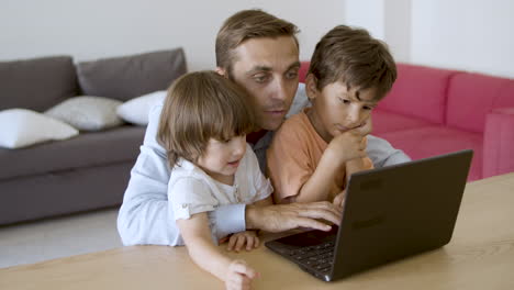 Focused-dad-hugging-sons,-using-laptop-and-talking