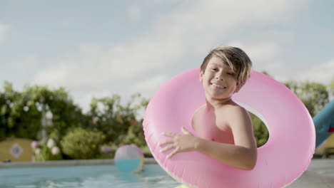 Boy-wearing-inflatable-ring,-sitting-on-poolside-and-smiling.