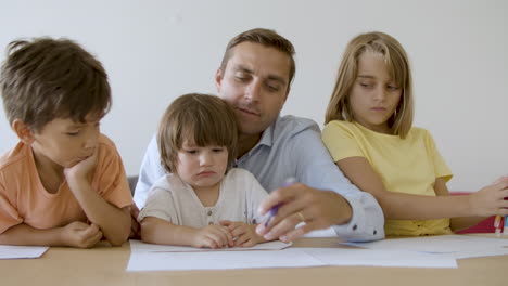Glücklicher-Vater,-Der-Mit-Kindern-Spricht-Und-Mit-Marker-Auf-Papier-Malt