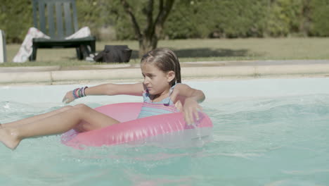 Cute-girl-swimming-in-big-inflatable-ring-in-open-air-pool.
