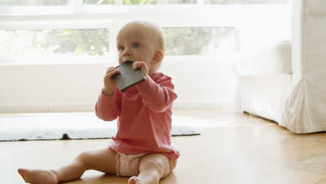 Lovely-baby-girl-sitting-on-floor-and-biting-smartphone