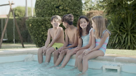 Children-sitting-on-poolside-splashing-their-feet-in-water.