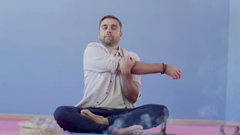 Man-sitting-in-lotus-pose-on-floor-in-studio-and-stretching-arms