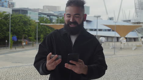Smiling-bearded-man-typing-card-number-on-smartphone-outdoor.