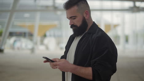 Focused-young-bearded-man-using-smartphone.