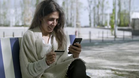 Smiling-middle-aged-woman-typing-card-number-on-smartphone.