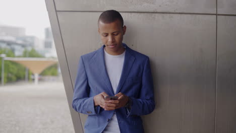 Smiling-young-man-leaning-on-wall-and-using-smartphone.