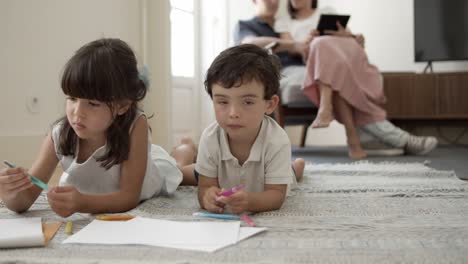 Pensive-little-boy-and-girl-with-markers-drawing-in-living-room