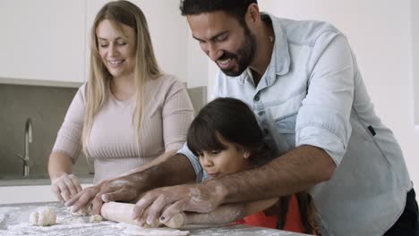 Young-parents-and-their-girl-kneading-and-rolling-dough