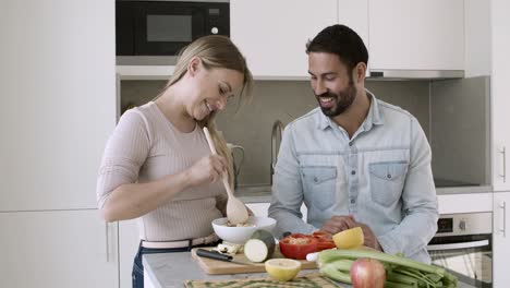 Cheerful-young-couple-cooking-salad-together
