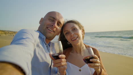 Couple-drinking-wine-and-smiling-at-camera-on-beach