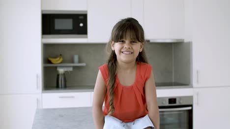 Cheerful-smiling-little-girl-sitting-on-kitchen-counter