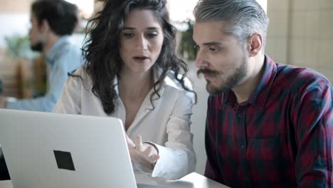 Focused-young-woman-working-with-confident-bearded-colleague