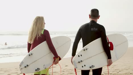 Back-view-of-couple-with-surfboards-walking-on-beach
