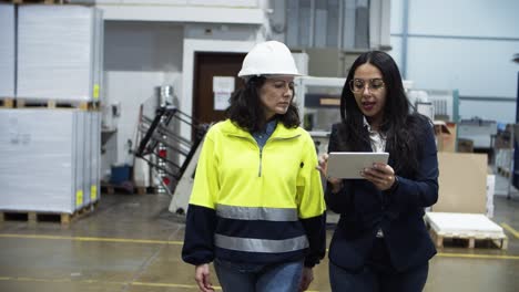 Two-female-workers-walking-with-tablet-at-factory