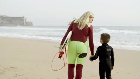 Mother-and-son-in-wetsuits-walking-on-beach