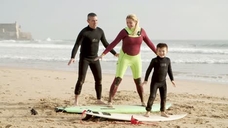 Family-lying-and-standing-on-surfboards-on-beach