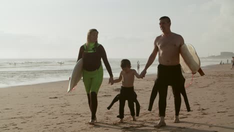 Family-with-surfboards-walking-on-sandy-beach