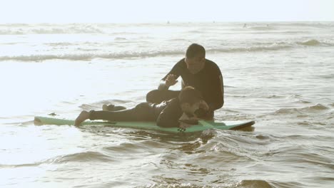 Father-teaching-son-standing-on-surfboard