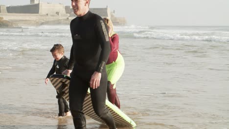 Parents-and-son-with-surfboard-on-beach