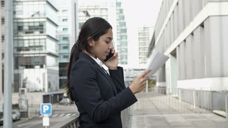 Businesswoman-holding-papers-and-talking-by-smartphone