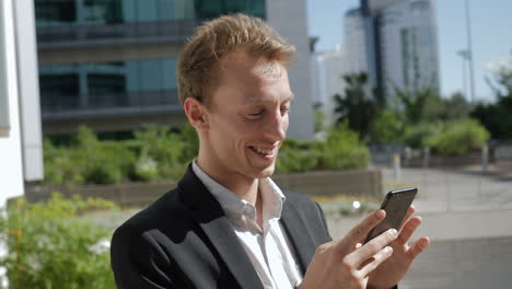 Young-Caucasian-man-texting-on-phone-outside,-laughing