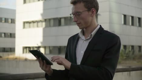 Good-looking-man-walking-outside,-working-on-tablet