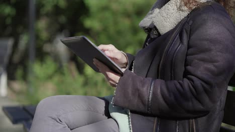 Cropped-shot-of-woman-wearing-warm-clothing-using-tablet-outdoor