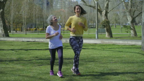 Two-women-jogging-in-park,-talking,-looking-happy