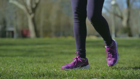Slim-female-legs-in-black-leggings-walking-on-grass-in-park