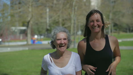Two-excited-women-jogging-in-park,-feeling-free,-raising-up-hand